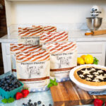 dried packaged strawberries and blueberries on wooden block with fresh berries and blueberry pie