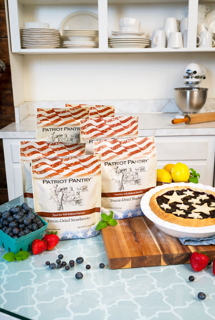dried packaged strawberries and blueberries on wooden block with fresh berries and blueberry pie