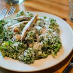 white bowl of Caesar salad with kale parmesan and anchovy sitting on wooden table at restaurant
