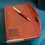 A Bedroc brown leather journal with a pen lying on a blue velvet couch for e-commerce and marketing.