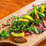 A cutting board with beef carpaccio topped with arugula peppers and jam served as appetizer