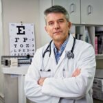 Dr. Parker Panovec wearing a lab coat standing in a clinic next to an eye chart
