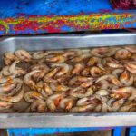 metal pan of freshly caught raw white shrimp in water on bright blue stand at food market in Ecuador