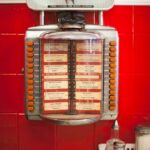 antique chrome jukebox with red buttons on red-tiled wall above table at Elliston Place Soda Shop.