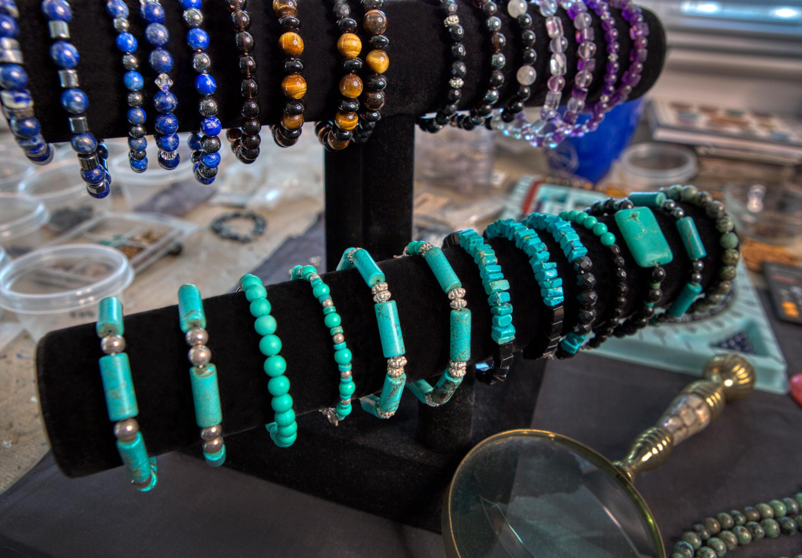 A variety of turquoise and other gemstone handmade bracelets on black display in an artist's studio