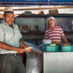 Two men one in Panama hat at a market stand selling freshly made peanut butter in Bahia de Caraquez