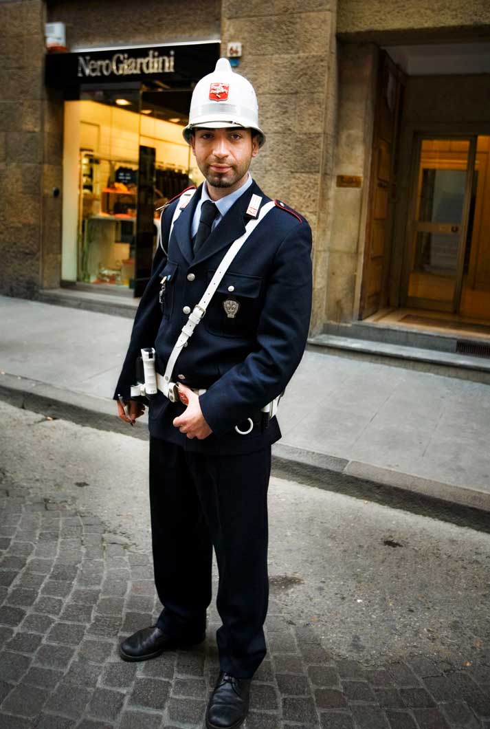 A young Italian policeman dressed in uniform holding his belt standing on a brick street in Florence