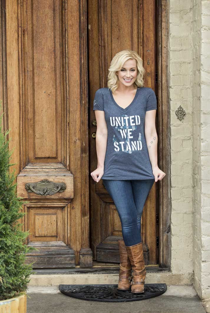 Kellie Pickler Wearing blue United We Stand USO T-Shirt standing at a large wooden front door