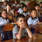Young kids in school uniforms in class with boy holding his mouth at Sri Sathya Sai Baba Ecuador
