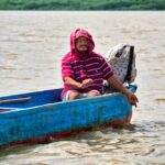 man in red and white striped shirt with his head wrapped fishing by hand in blue boat on Chone River