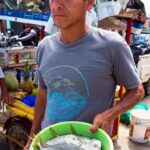 man in hat and t-shirt holding bright green pan of moonfish at open air market in Bahia de Caraquez