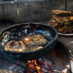 Freshly caught and pan fried fish cooked in a large black skillet outside in an open fire pit