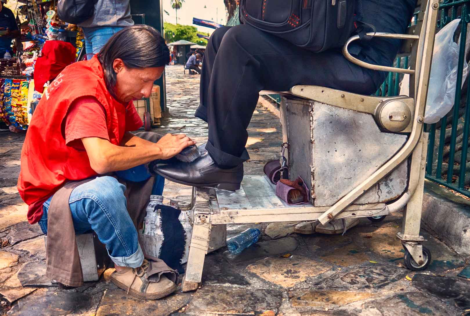 shoe shine vendor in red shirt shining man's shoes on street near Parque Seminario Park in Guayaquil