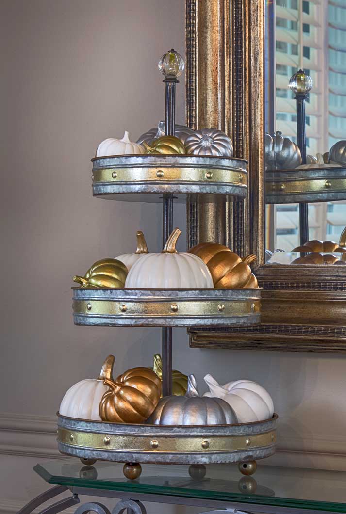 tin 3-tier home decor display stand with fall porcelain pumpkins on glass table next to mirror