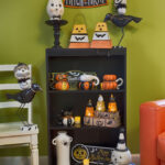 orange yellow white black Halloween holiday home decor products on bookshelf in room with green wall