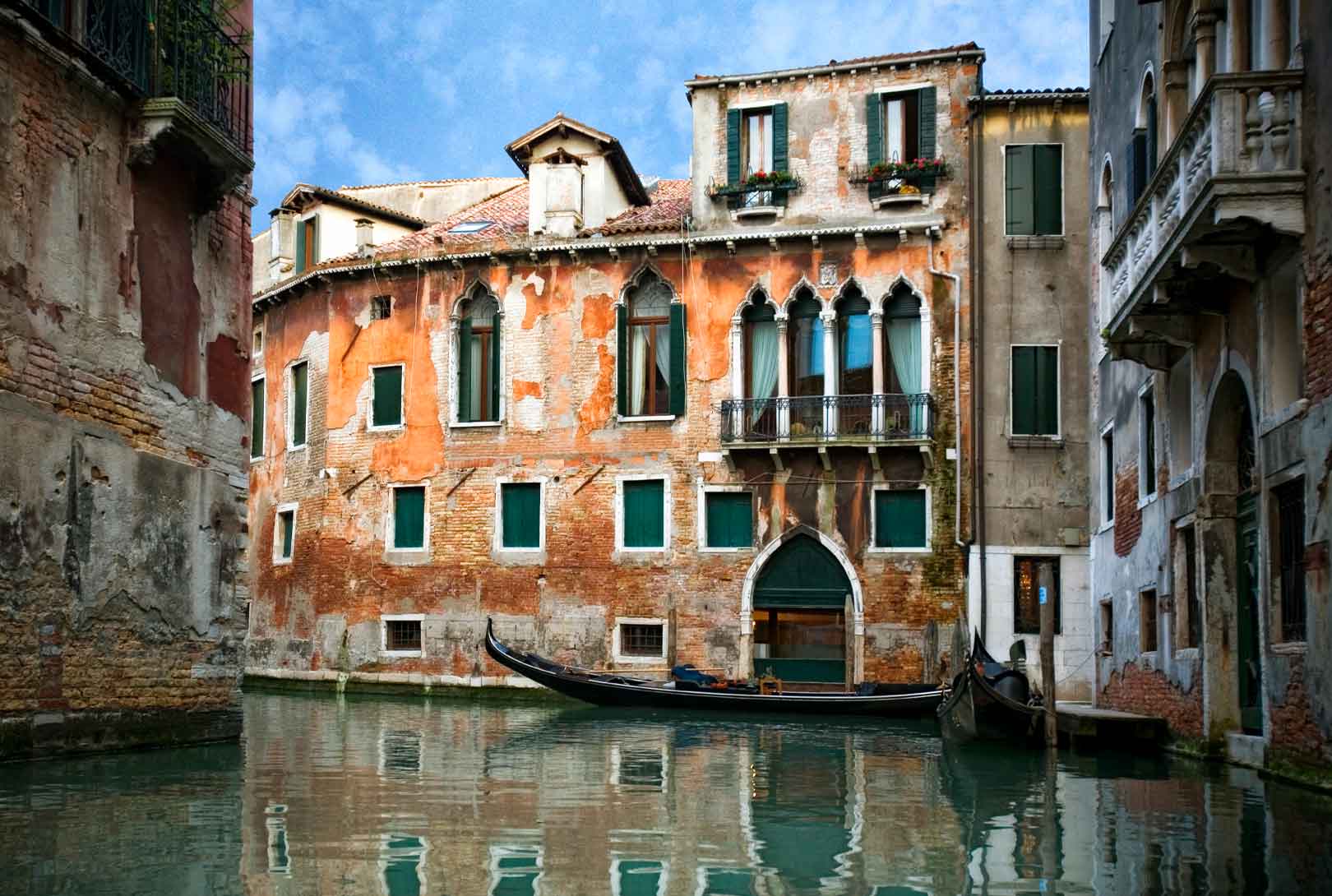 two Venetian gondolas tied outside stone buildings of different terracotta hues along a canal