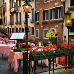 outdoor restaurant in Venice Italy on canal with planters of red flowers and pink tablecloths