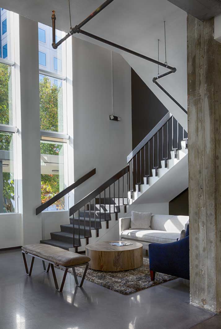 industrial loft-style office waiting area with a staircase and concrete walls and floors