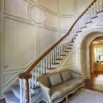 curved staircase with polished wood railing painted white wood accented walls, gray carpets, oak flooring, and gray couch
