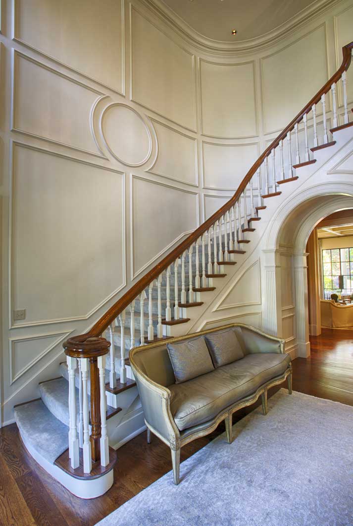 curved staircase with polished wood railing painted white wood accented walls, gray carpets, oak flooring, and gray couch