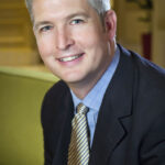 executive headshot of a male executive in suit with gold tie in room with c=green couch