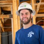 white male with beard in white hard hat and blue shirt in home under construction