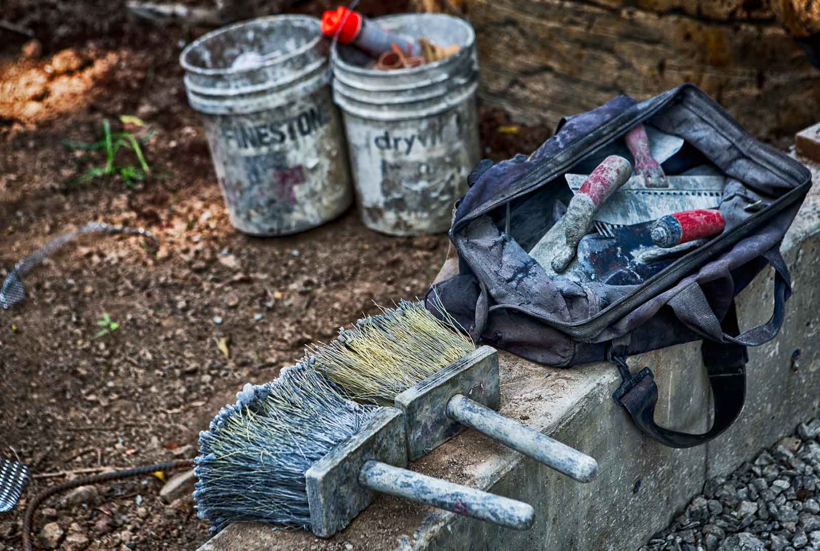two white buckets two concrete brush tools a bag of other tools sitting on an outdoor ledge