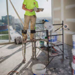 young male construction worker on stilts holding a troth of drywall mud