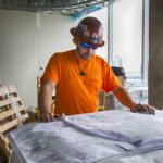 male construction manager in orange t-shirt and safety glasses looking at blueprints