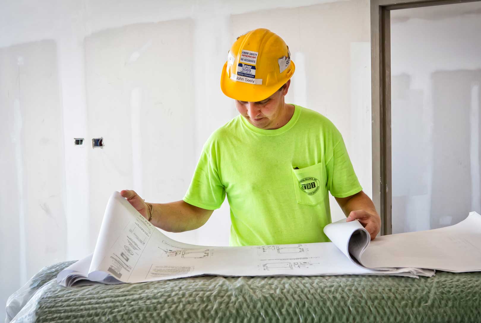 a male construction worker in yellow hardhat looking over blueprints