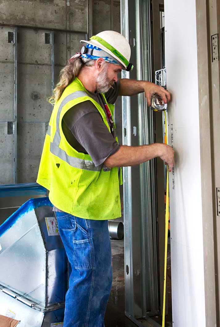 bearded construction worker measuring wall with tape measure