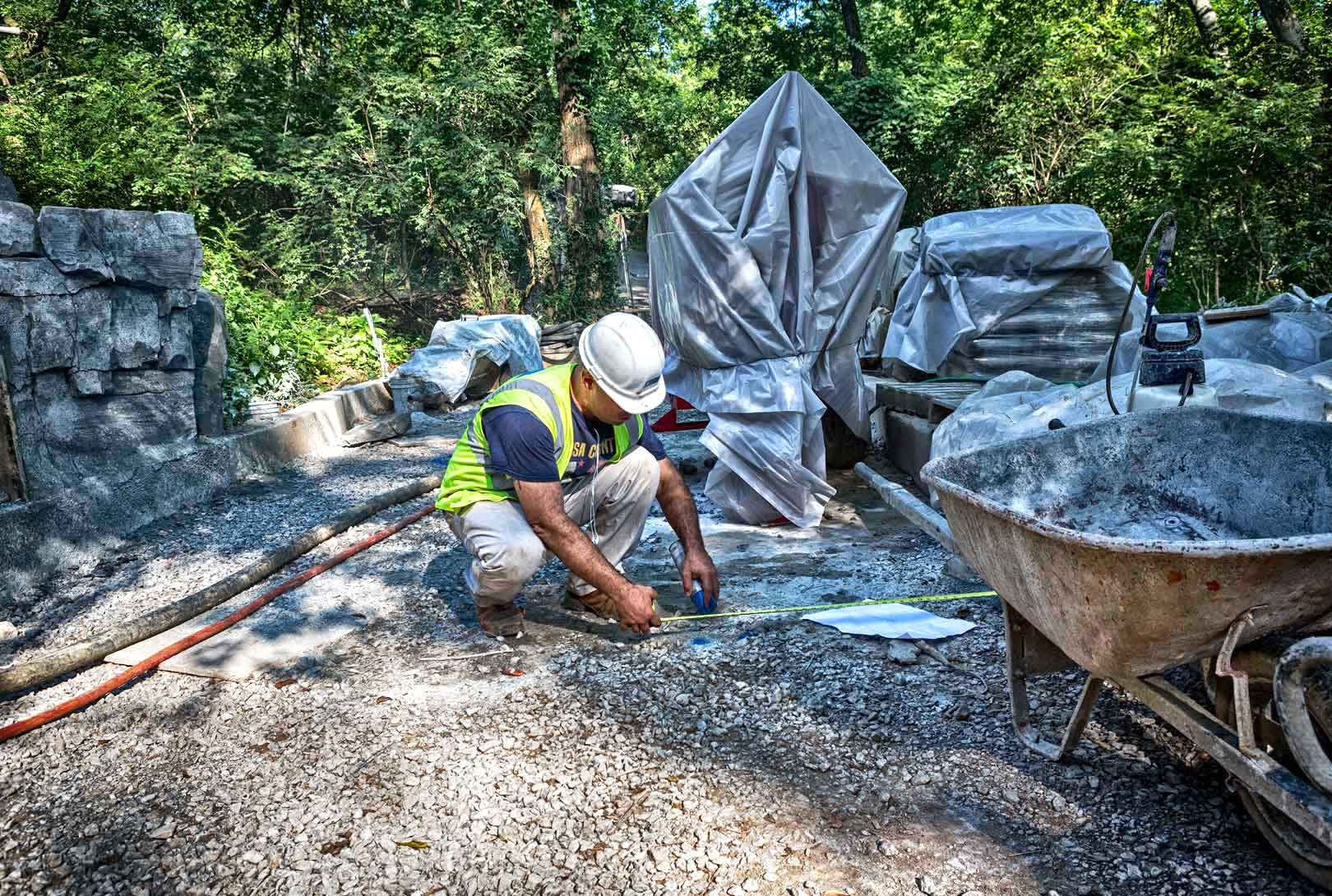 construction worker marking a tape-measured spot with blue spray paint on a gravel path