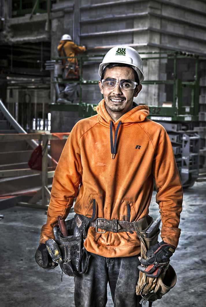 portrait of young ethnic male construction worker wearing tool belt and safety glasses a