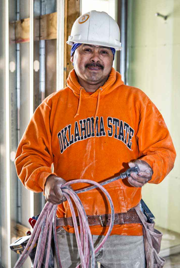 male construction worker with mustache in orange Oklahoma state sweatshirt holding extension chord