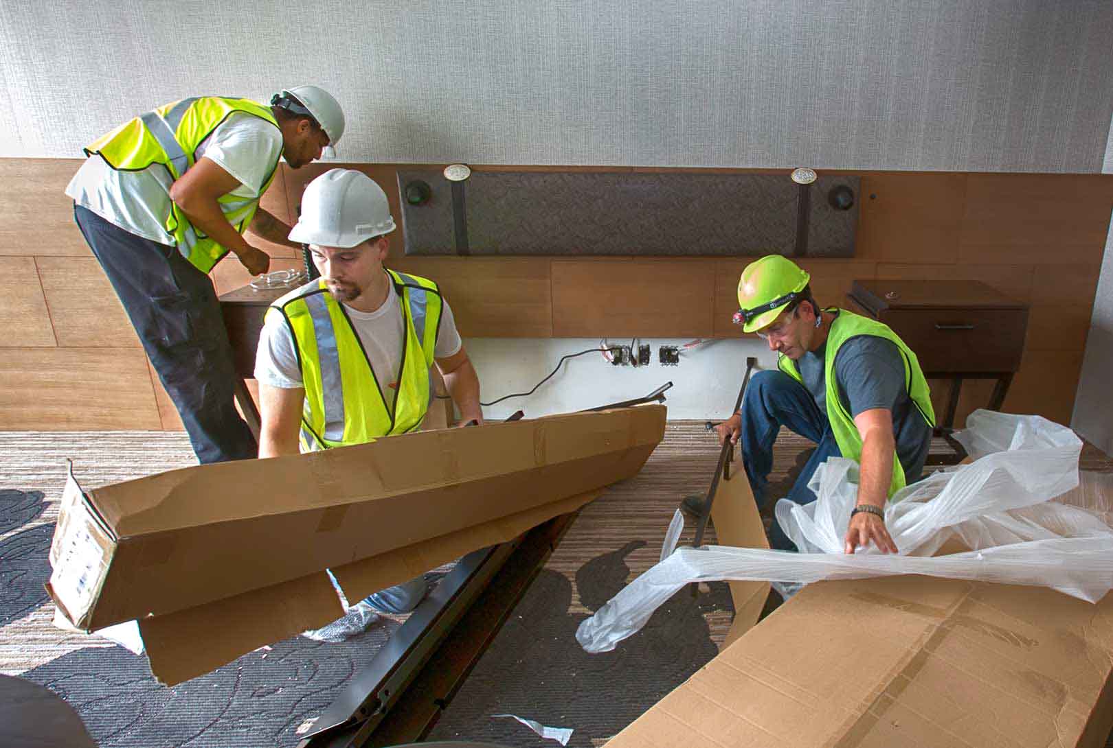 three construction workers unpack and assemble furniture while staging newly built hotel room