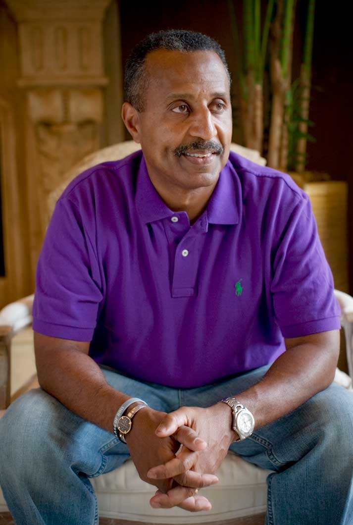 middle aged african american man sitting in a white chair wearing a purple shirt in his home