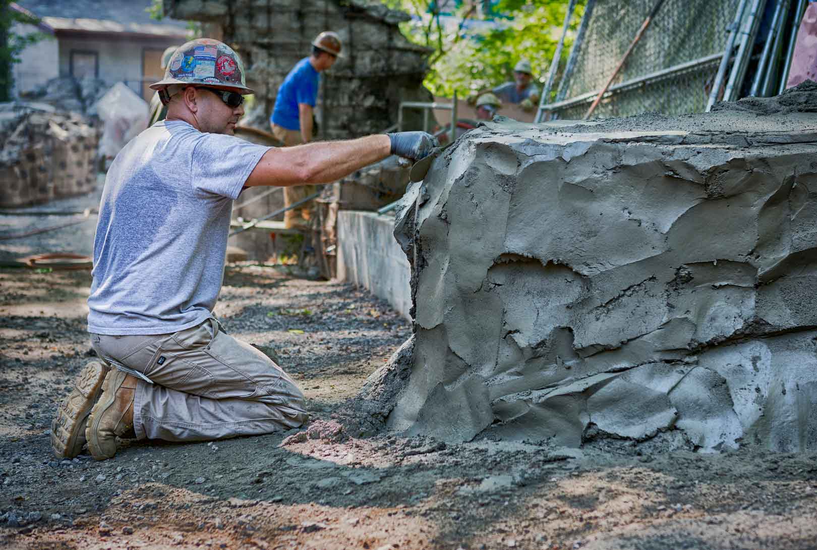 male construction worker hand trowels concrete into rock formations at zoo