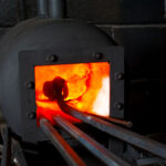 orange glowing open furnace with a metal ram head being heated up