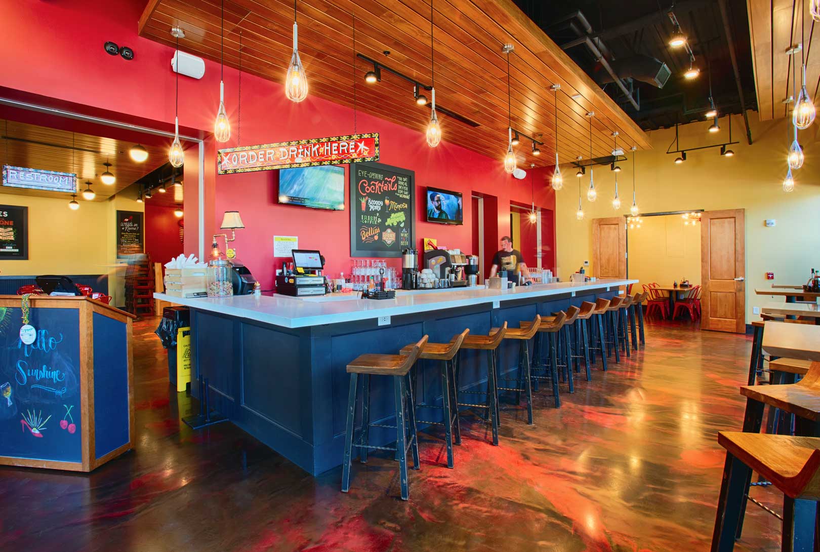 bar area of restaurant entrance with red and yellow walls, blue-gray wood bar and wooden stools