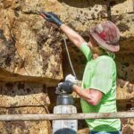 male concrete worker in green shirt and hard hat staining fabricated rock formation