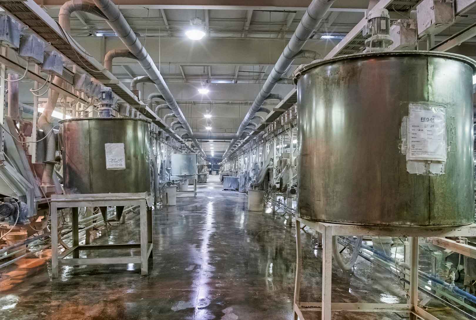 inside of tile manufacturing warehouse with rows of machinery, tanks, and hoses