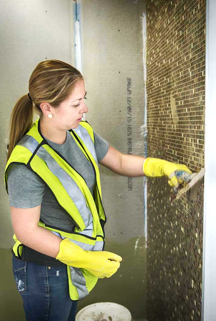 female tile worker in a ponytail spreading grout over tile
