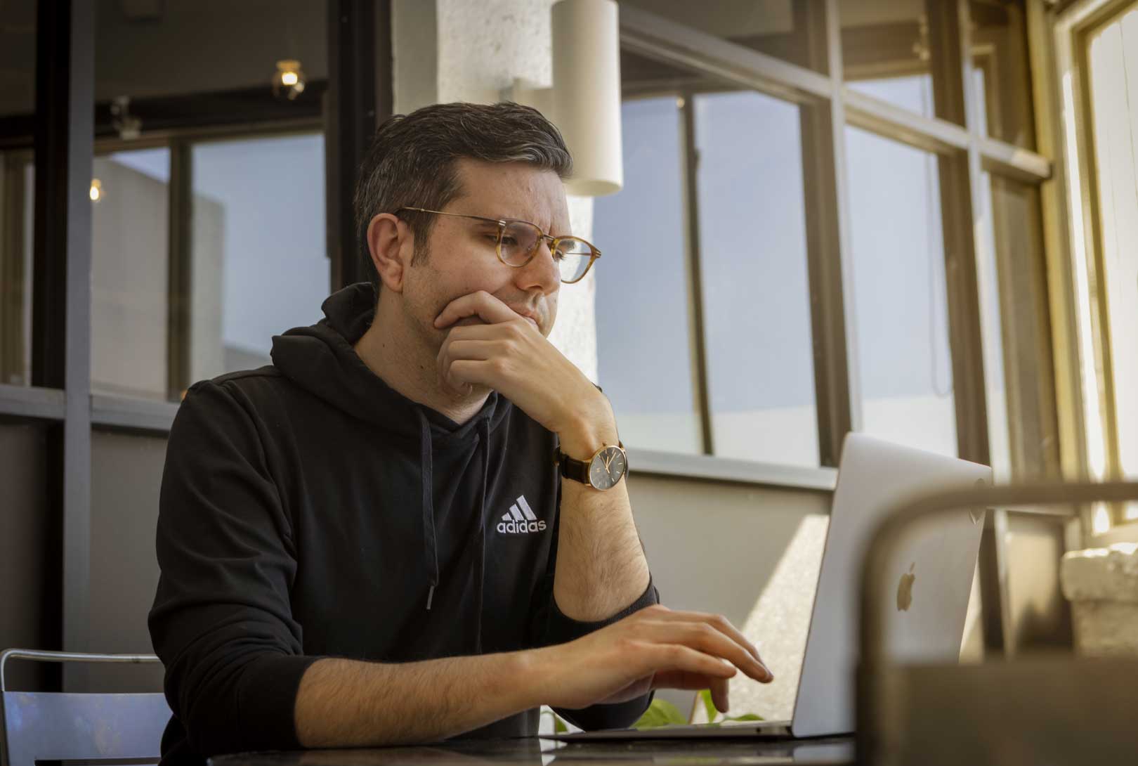 Travis Terrell wearing a black Adidas sweatshirt sitting working on his laptop