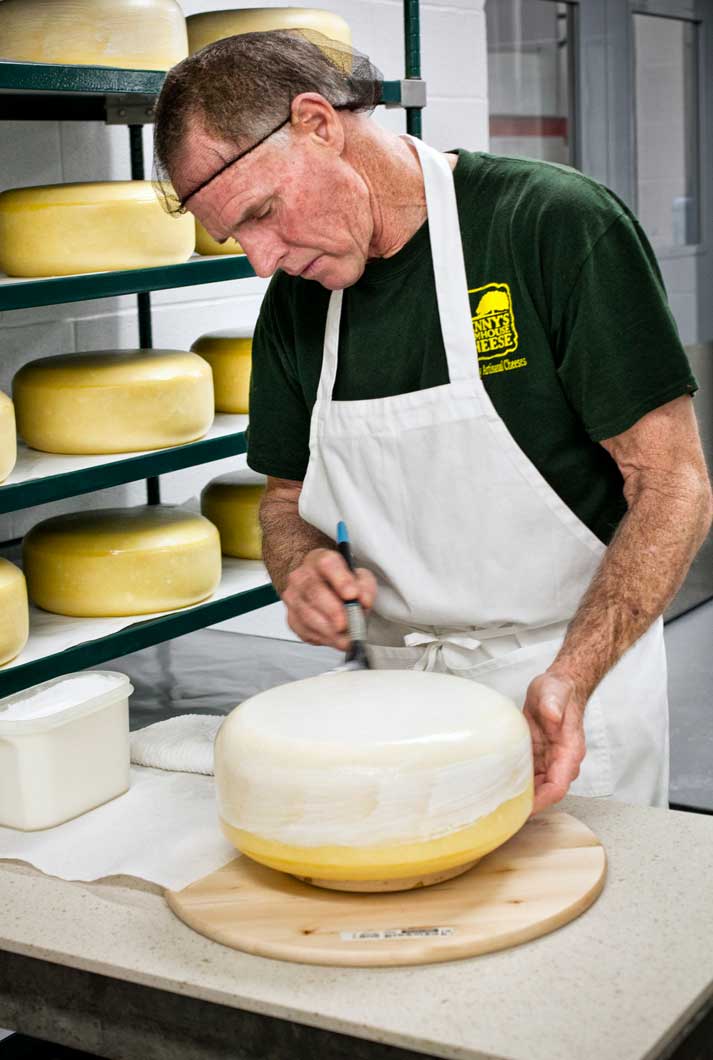 man waxing large round block of cheese