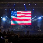 An American flag on a large screen in an indoor stadium at a rehearsal sound check