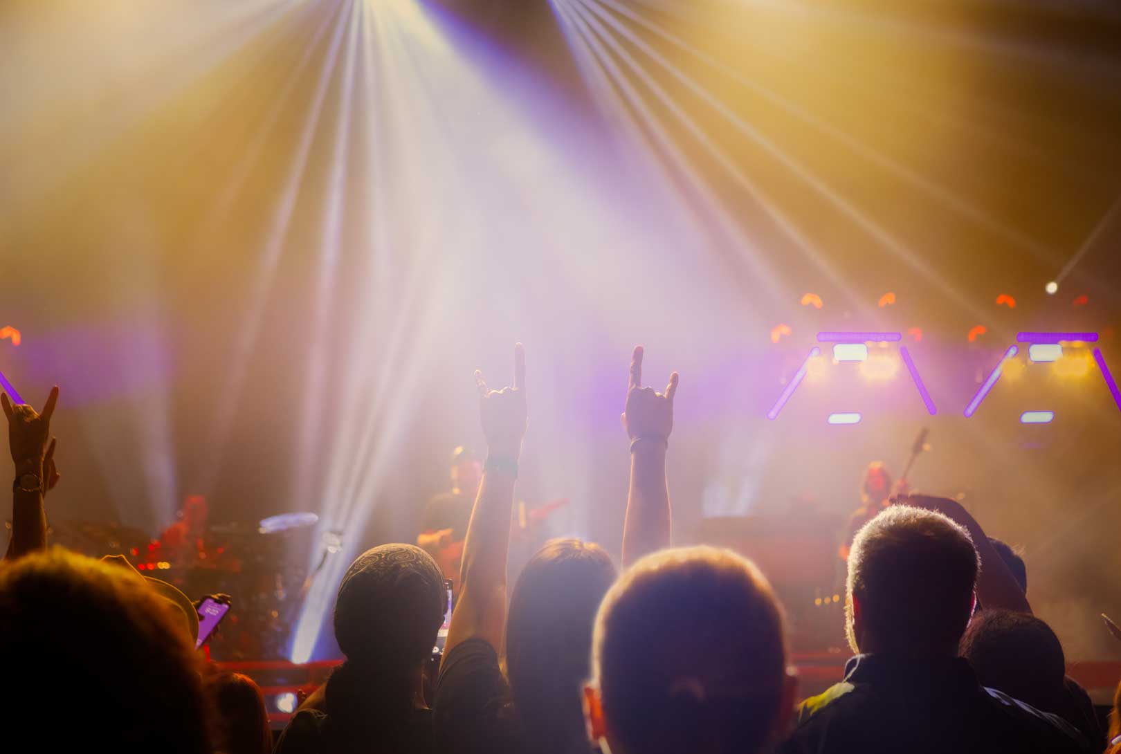 audience in front of stage with hands in the air at live music concert with streams of stage lights