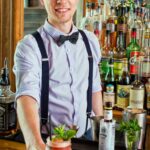 Graham "Guice" Fuze in suspenders and bow tie behind bar with speciality drink