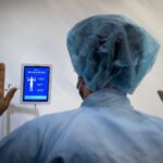 worker in hairnet holding hands up for optical AI recognition machine scan at healthcare facility
