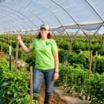 farmer Amy Delvin standing in a greenhouse near an organic crop of greens