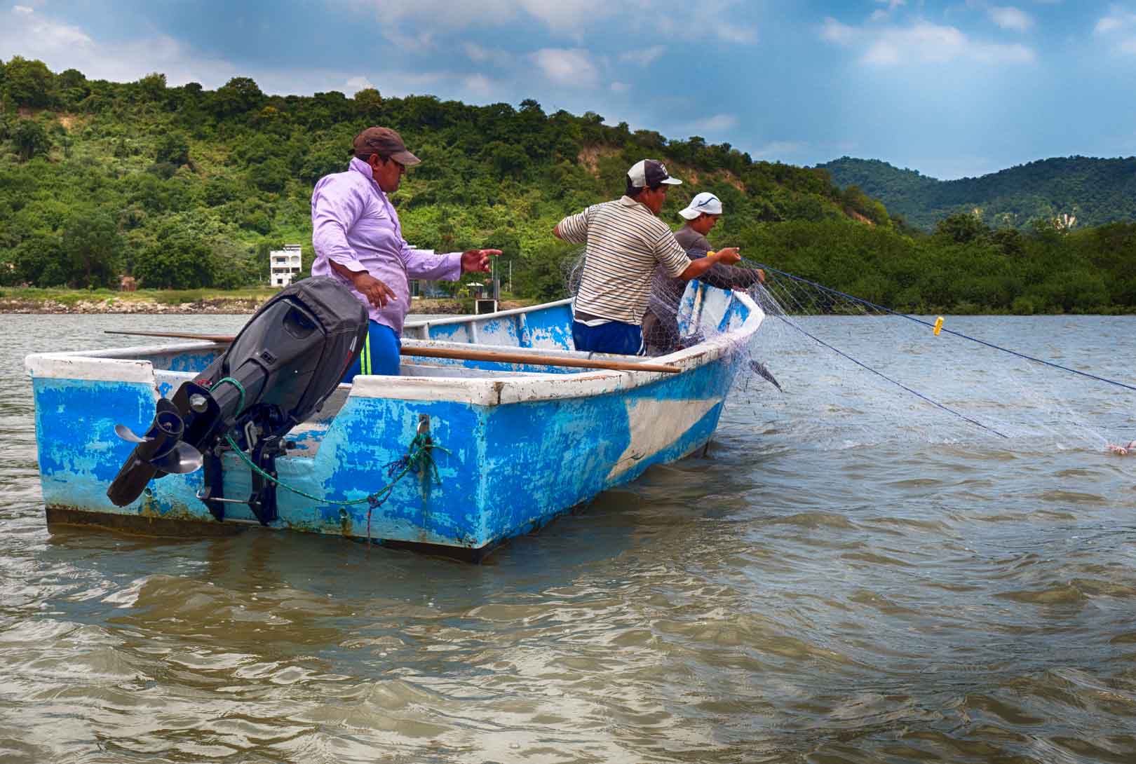Two fishermen pulling in fishing nets on blue boat on the Chone River in Bahia de Caraquez Ecuador